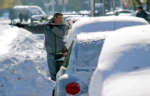 Мужчина ждёт прогрева двигателя и очищает от снега автомобиль